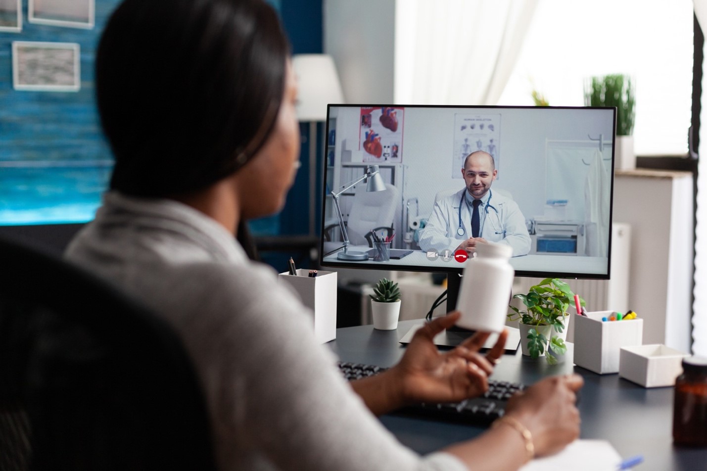 Woman holding medicine bottle on a video call with doctor on computer